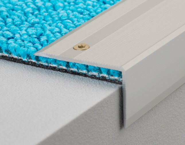 Close-up of blue carpet edge with aluminium threshold on a step.