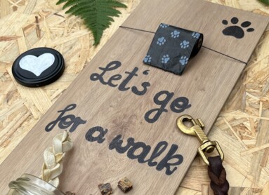 Eine Tafel mit der Aufschrift "Let's go for a walk", Hundekotbeutel, Leine und Leckerlis auf Laminatboden.
