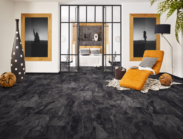 Living room with dark laminate flooring, featuring an orange chaise lounge, decorative vases, and large framed photographs.