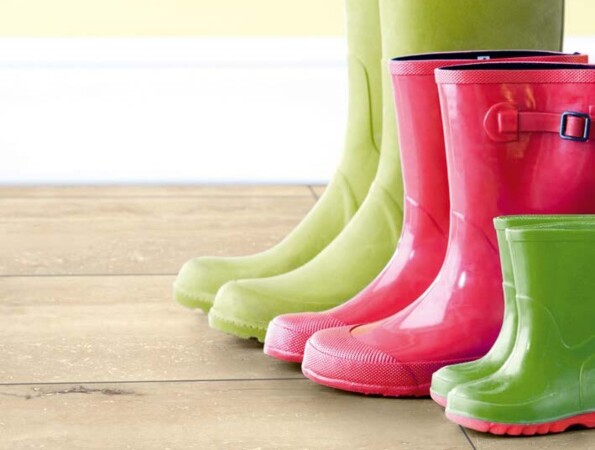 Bunte Gummistiefel auf einem Laminatboden vor einer gelben Wand.