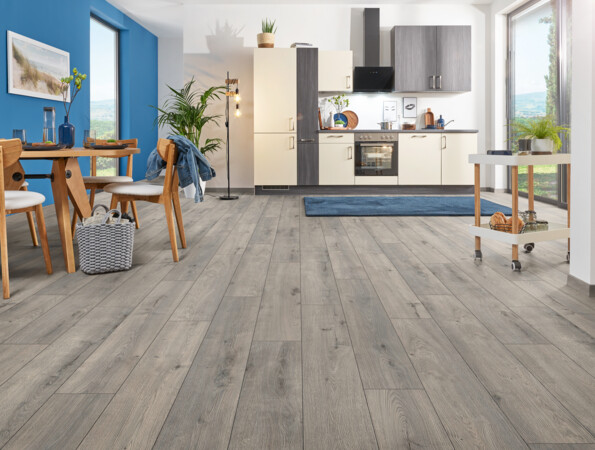 Moderne Küche mit blauem Akzent, Feuchtraumboden der Serie 'Aquaprotect smart' und Essbereich mit Holzmöbeln, großen Fenstern und Pflanzen.
