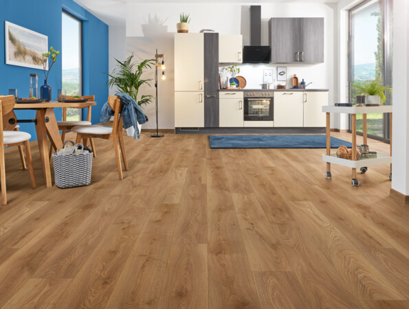 Moderner Küchen- und Essbereich mit hellem Laminatboden der Serie 'Aquaprotect Smart Silent' und blauer Wand, Holzmöbeln und großen Fenstern.