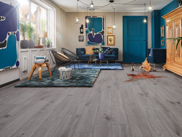 Spacious living room with grey laminate flooring, blue accents, wooden furniture, and abstract art on the walls.