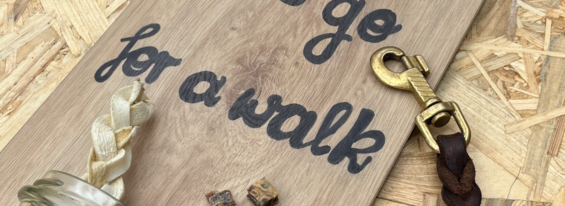 Eine Tafel mit der Aufschrift "Let's go for a walk", Hundekotbeutel, Leine und Leckerlis auf Laminatboden.
