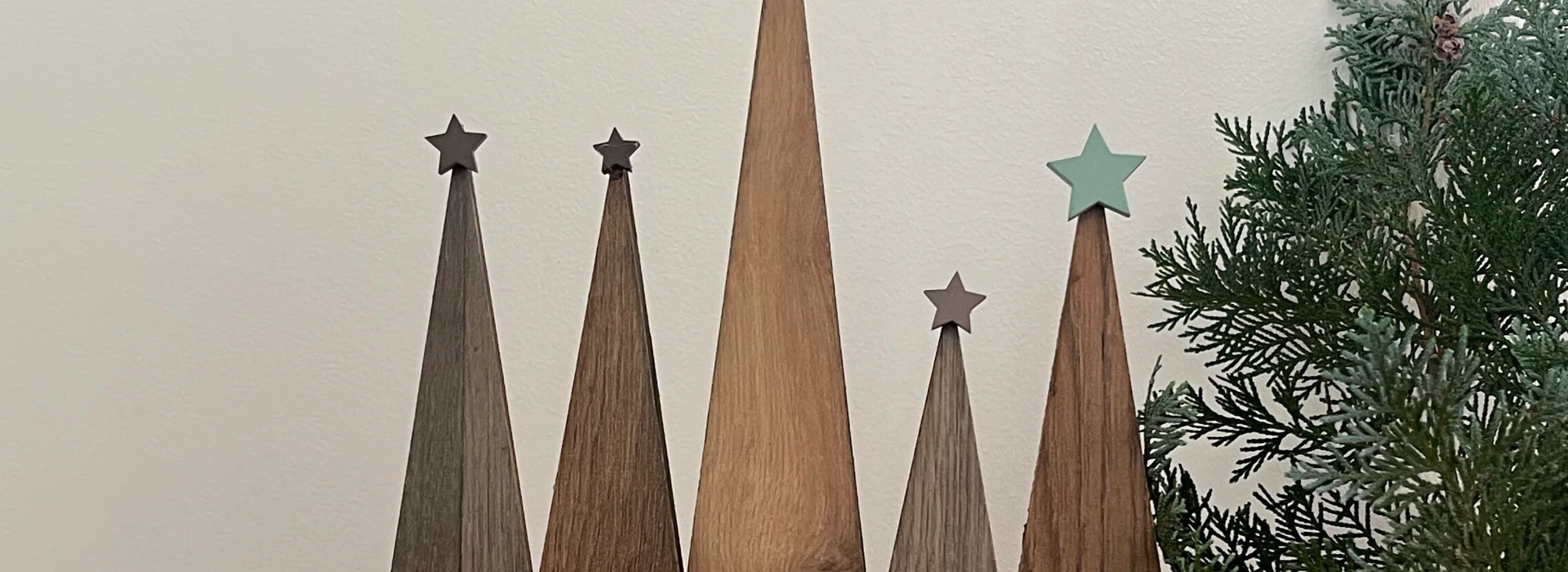 Dekoration mit Holz-Weihnachtsbäumen, grünem Zweig und Kerze auf Teppich.