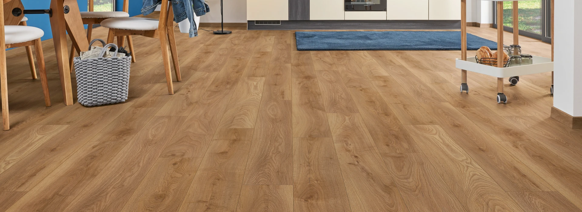 Moderner Küchen- und Essbereich mit hellem Laminatboden der Serie 'Aquaprotect Smart Silent' und blauer Wand, Holzmöbeln und großen Fenstern.