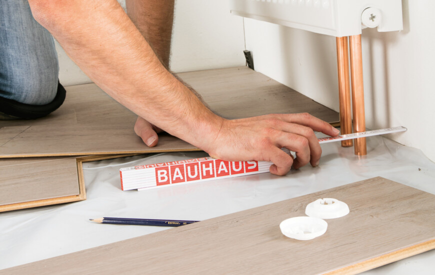 Ein Handwerker misst Laminatboden aus und verwendet dabei einen Zollstock von BAUHAUS.