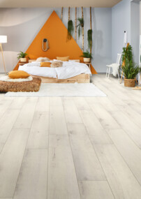 Schlafzimmer mit hellem Laminatboden, gemütlichem Bett und Pflanzen.