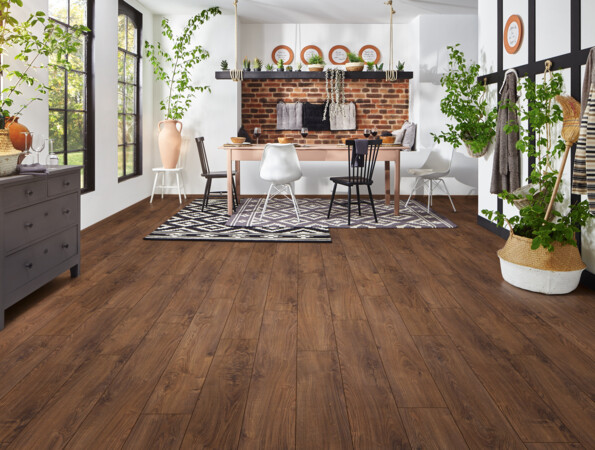 Spacious room with laminate flooring, white walls, large windows, plants, and a dining area featuring a brick accent wall and stylish decor.