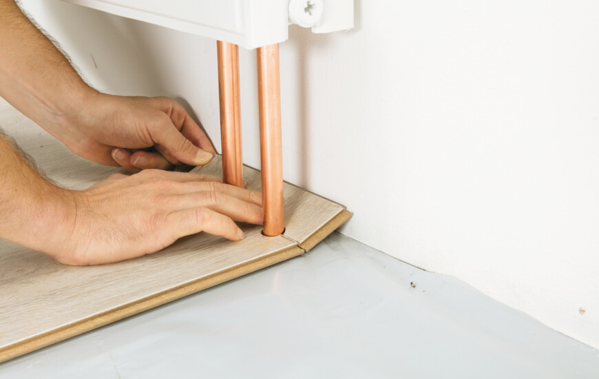 Hände installieren Laminatboden um Heizungsrohre.