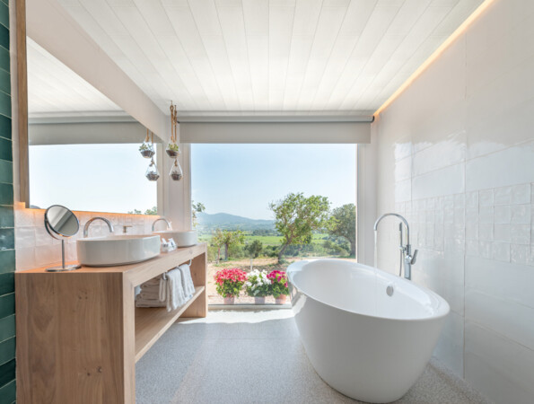 Modernes Badezimmer mit freistehender Badewanne und Blick auf die Natur durch ein großes Fenster, mit stilvollen Oberflächen und eleganter Einrichtung.