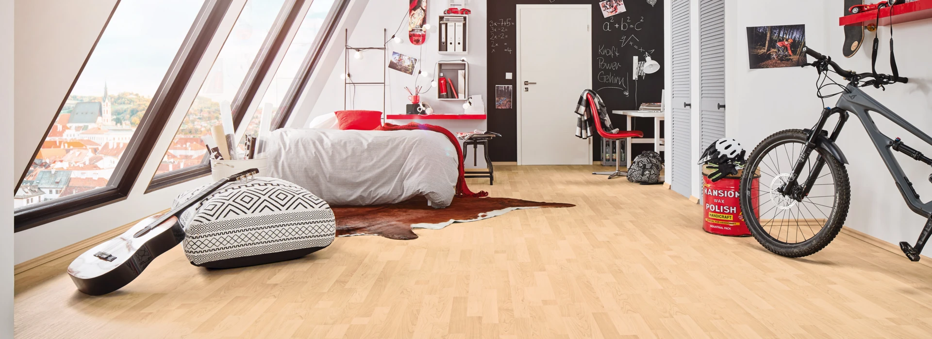 Attic bedroom with light laminate flooring, featuring a bed, desk, guitar, and bicycle near large windows.