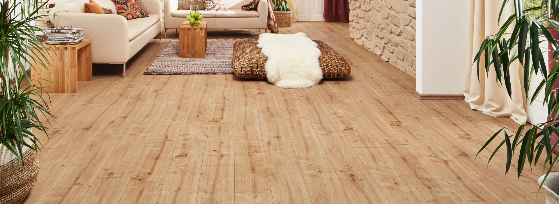 Helles Wohnzimmer mit stilvollem Laminatboden der Serie 'Vinto', gemütlichen Sofas, Pflanzen und dekorativen Elementen für eine einladende Atmosphäre.