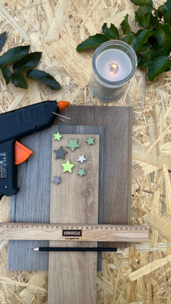 Heißklebepistole, Kerze, Lineal, Bleistift und Sterne auf Laminatbodenmuster.