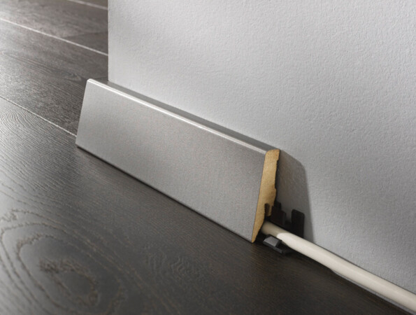 Sockelleiste aus Holz, die Kabel auf dunklem Laminatboden verdeckt.