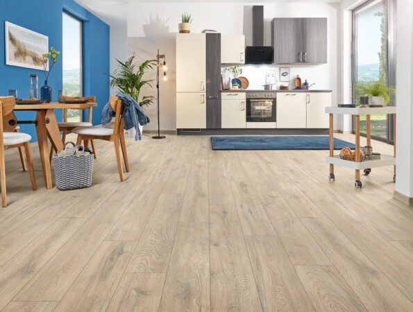 Offene Küche mit hellem Laminatboden, Esstisch, blauer Wand und viel natürlichem Licht.