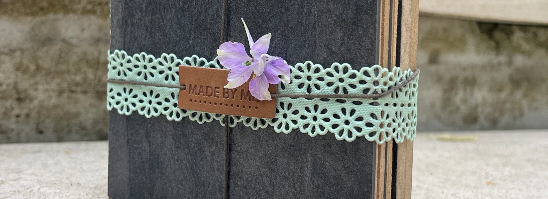 Kleines Buch mit grünem Spitzenband und Blume, im Freien auf Steinoberfläche platziert.