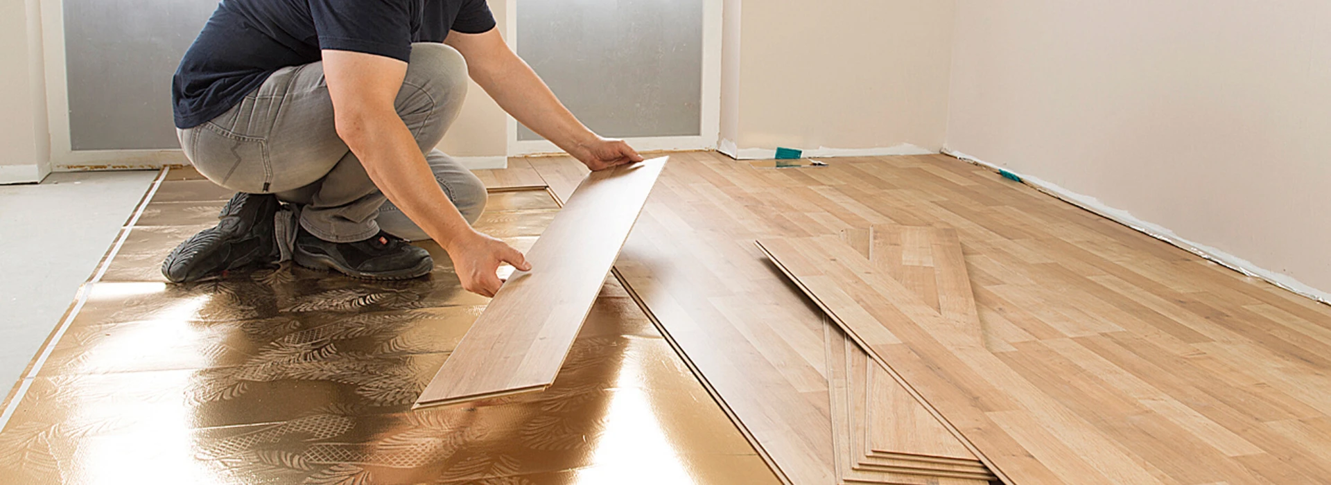 Ein Mann verlegt Laminatboden in einem Raum mit hellem Holzdesign.
