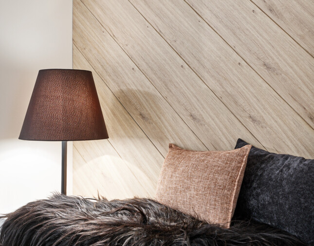 Cosy corner with a lamp, textured cushions, and a black fur throw, featuring wall panels in the background.