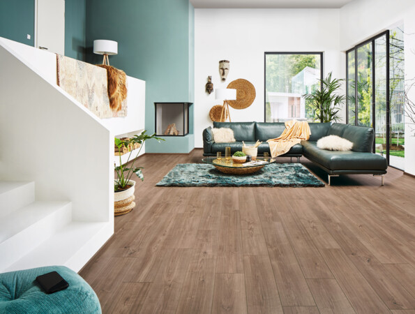 Modernes Wohnzimmer mit grüner Ledercouch, Laminatboden der Serie 'Vinto', großem Fenster und Dekorationen.
