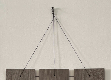 Wanddekoration mit Fotos und Karten auf Holzpaneelen, darunter ein Regal mit Keramikfigur und Stiftehalter.