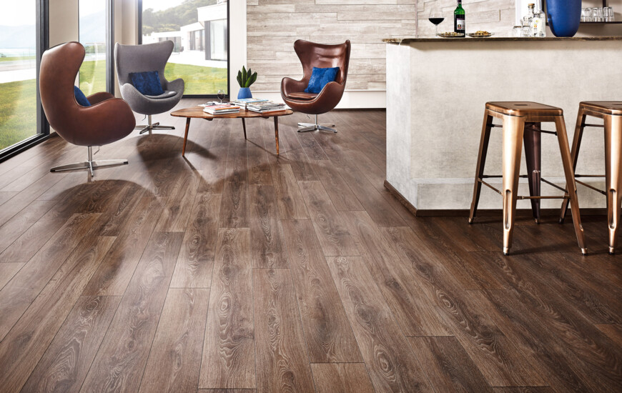 Stylish room with laminate flooring, featuring modern chairs, a coffee table, and a bar area with stools, illuminated by large windows.
