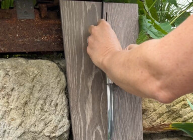 Eine Hand zieht einen Löffel aus einer Halterung an einer Holzplatte, umgeben von Pflanzen. Laminatboden sichtbar.