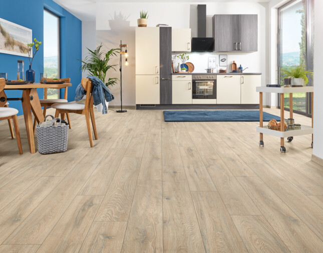 Open kitchen with light laminate flooring, dining table, and large windows.