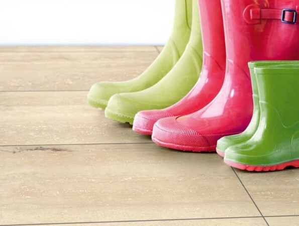 Bunte Gummistiefel auf einem Laminatboden vor einer gelben Wand.