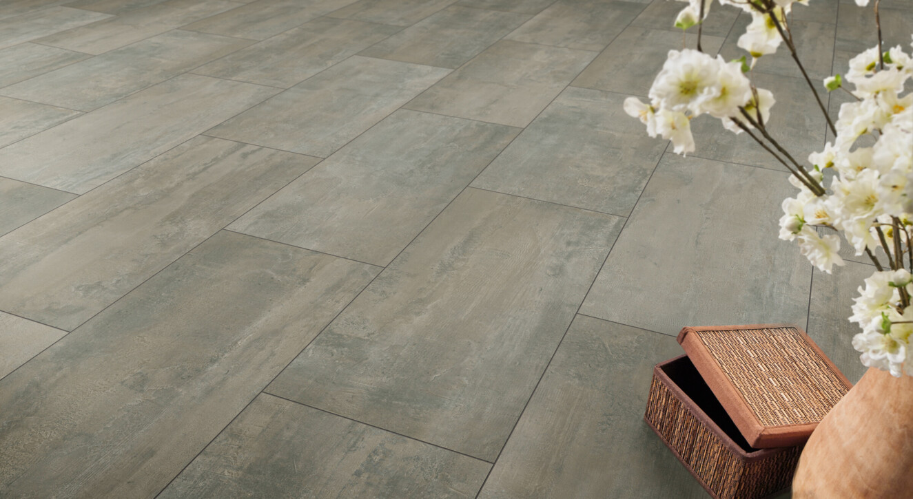 Laminate flooring with a textured stone appearance, featuring a vase with white flowers and an open woven box on the floor.