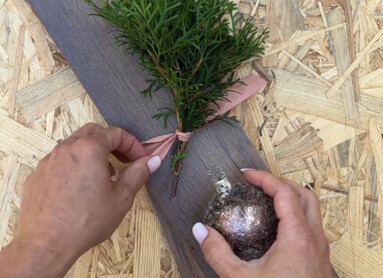 Eine Hand dekoriert Laminatboden mit einem Zweig und einer glänzenden Kugel.