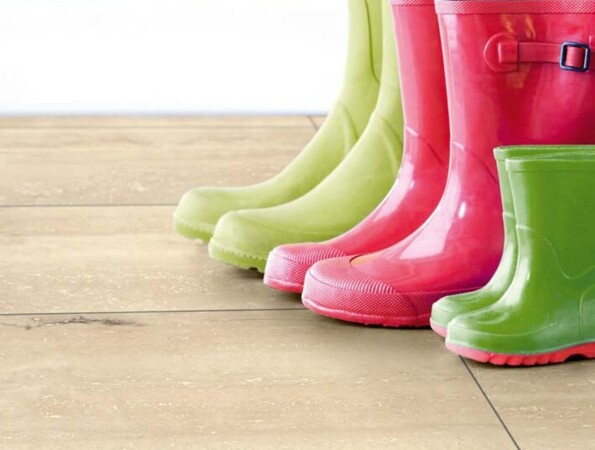 Bunte Gummistiefel auf einem Laminatboden vor einer gelben Wand.