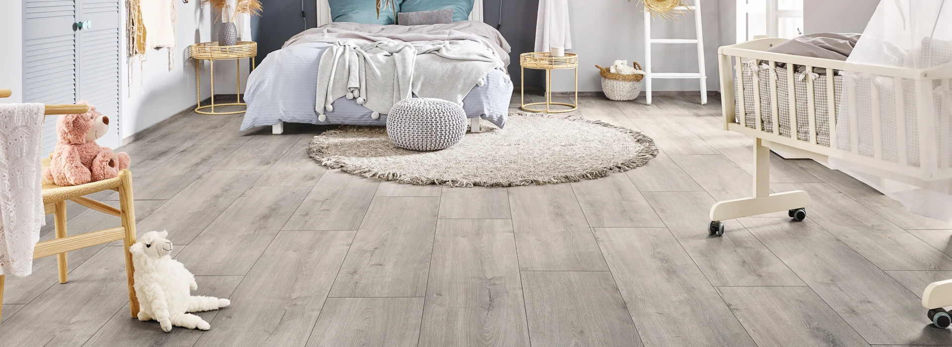 Helles Schlafzimmer mit grauem Laminatboden der Serie 'Vinto' und gemütlicher Dekoration, einschließlich Himmelbett, Babybett und Spielzeug.