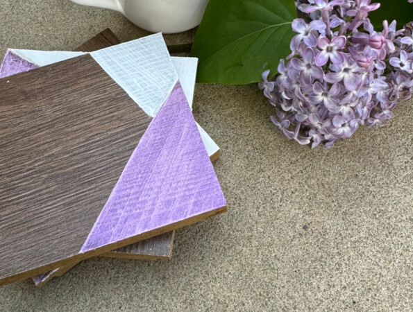 Kaffeetasse neben Fliederblüten und dekorativen Laminatbodenmustern auf Beton.