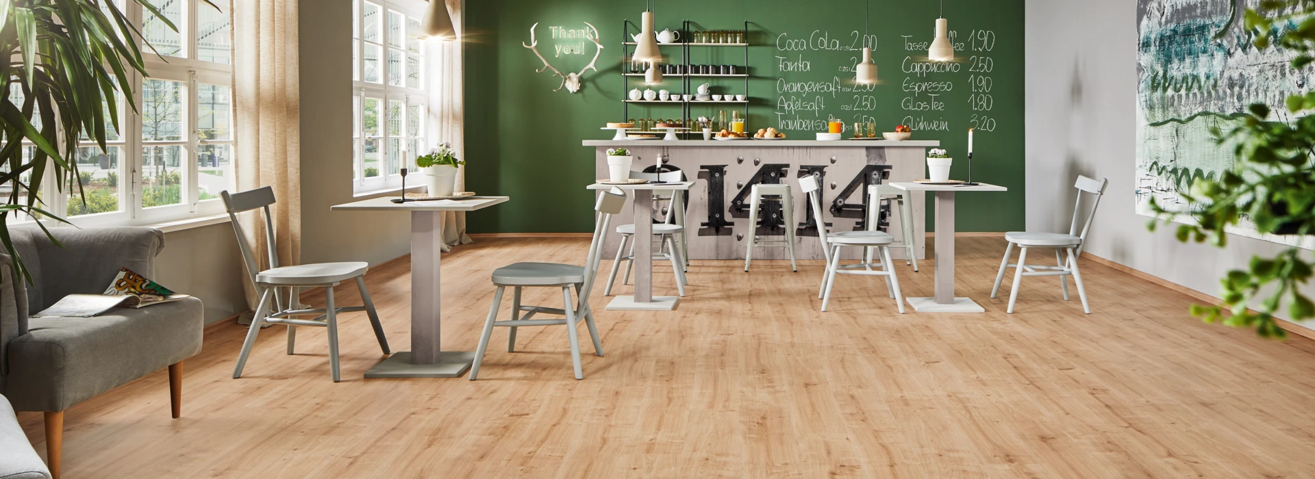 Gemütliches Café mit hellem Laminatboden der Serie 'Ambienta', modernen Möbeln und grüner Wand im Hintergrund.