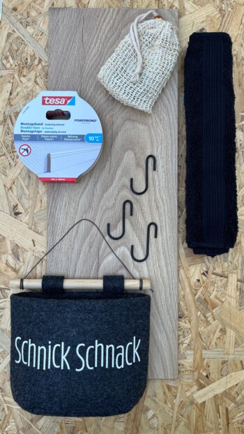 Verschiedene DIY-Materialien auf Holzplatte, darunter Tesa-Klebeband und Filztasche mit "Schnick Schnack"-Aufschrift.