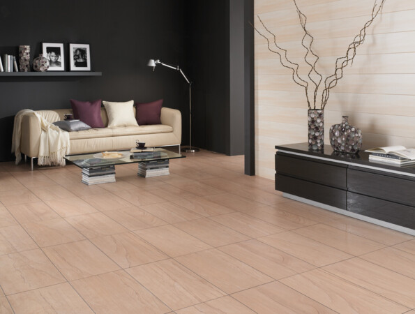 Wohnzimmer mit hellem Boden, cremefarbenem Sofa, Glastisch, und dekorativen Vasen auf schwarzem Sideboard. An der Wand befinden sich helle Wandpaneele.