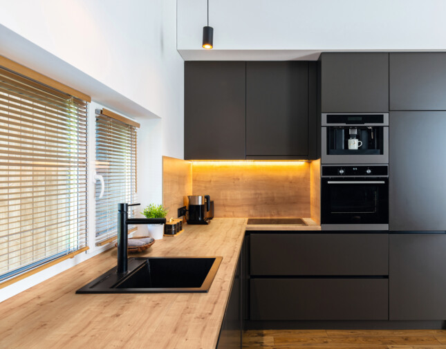 Moderne Küche mit Arbeitsplatte 'elementa', schwarzen Schränken, eingebautem Ofen und Laminatboden.