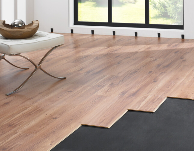 Laminate flooring installation in progress near a large window, showcasing partially laid planks and underlayment.