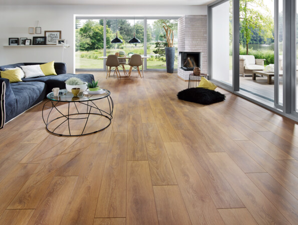 Spacious living room with light laminate flooring, large windows, and a cosy seating area overlooking a garden.