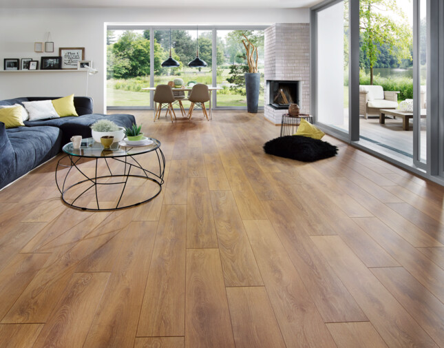 Spacious living room with light laminate flooring, large windows, and a cosy seating area overlooking a garden.