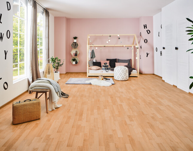 Room with light laminate flooring, pink accent wall, and cosy decor including a bed with string lights, pouffe, and plants by a large window.