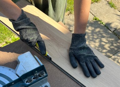 Eine Person schneidet Laminatboden mit einer Kreissäge im Freien.