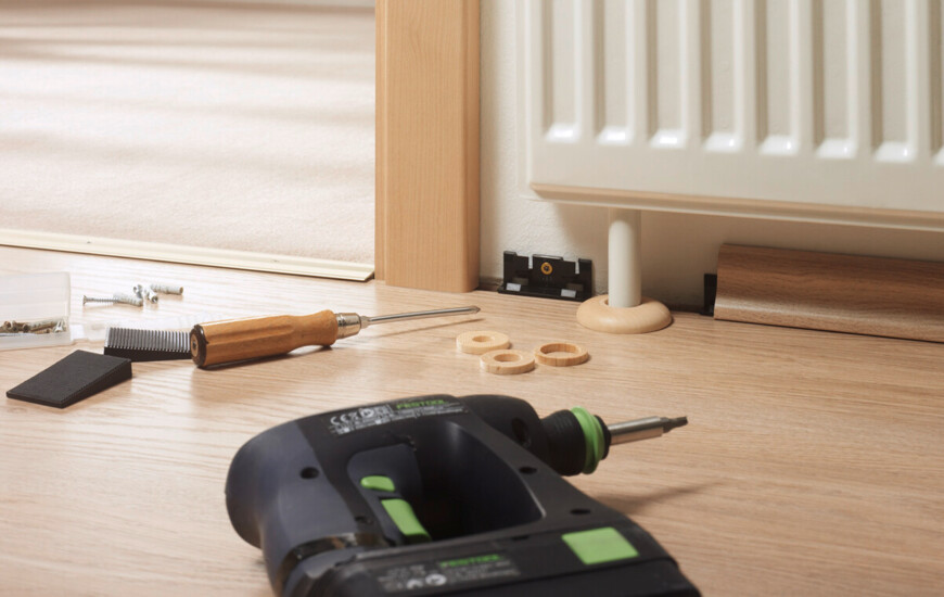 Werkzeuge und Materialien zur Installation von Laminatboden neben einem Heizkörper.