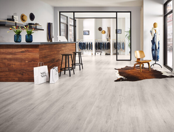 Moderner Raum mit hellem Laminatboden, Holztresen, Schaufenster und Kleiderständer.