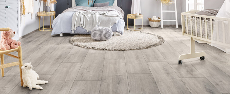 Helles Schlafzimmer mit grauem Laminatboden der Serie 'Vinto' und gemütlicher Dekoration, einschließlich Himmelbett, Babybett und Spielzeug.