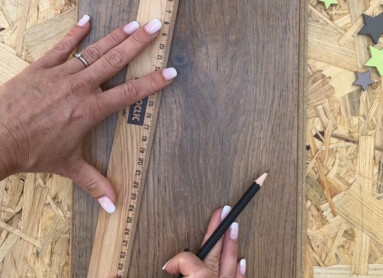 Eine Person misst ein Stück Laminatboden mit einem Lineal und Bleistift, daneben brennt eine Kerze.