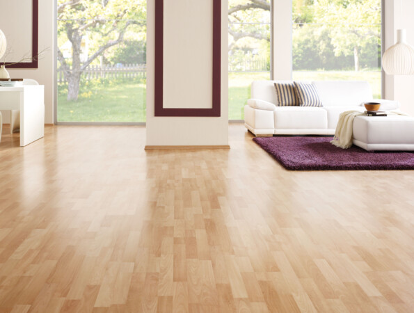 Living room with light laminate flooring, white furniture, and large windows overlooking a garden.