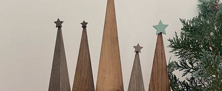 Dekoration mit Holz-Weihnachtsbäumen, grünem Zweig und Kerze auf Teppich.