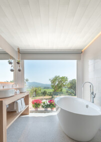 Modernes Badezimmer mit freistehender Badewanne und Blick auf die Natur durch ein großes Fenster, mit stilvollen Oberflächen und eleganter Einrichtung.